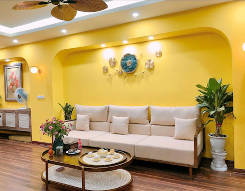 Tâm điểm của không gian phòng khách mẫu thiết kế căn hộ 90m2 là bộ sofa trắng và bức tường vàng