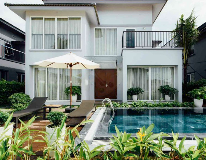 Mẫu biệt thự nghỉ dưỡng mini 2 tầng mái bằng phong cách hiện đại có hồ bơi trước nhà, bên cạnh là 2 chiếc ghế nằm tắm nắng 